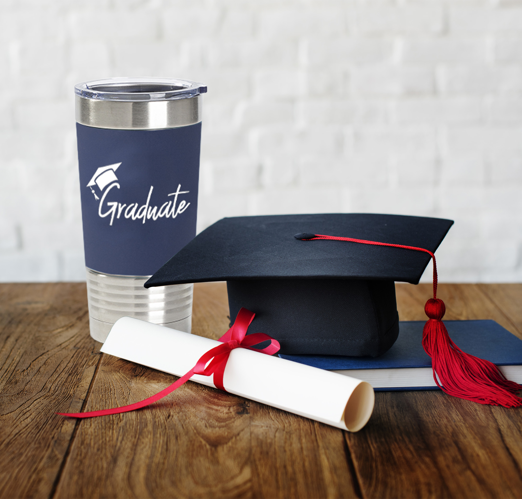 tumbler personalized with graduate on a table next to cap, scroll, and book